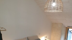 A bedroom with a large bed, a hanging light fixture, and a nightstand with a lamp. - House (Neulliac)