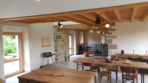 A spacious living area with a stone wall, wooden ceiling beams, a sofa, and a dining table with chairs. - House (Neulliac)