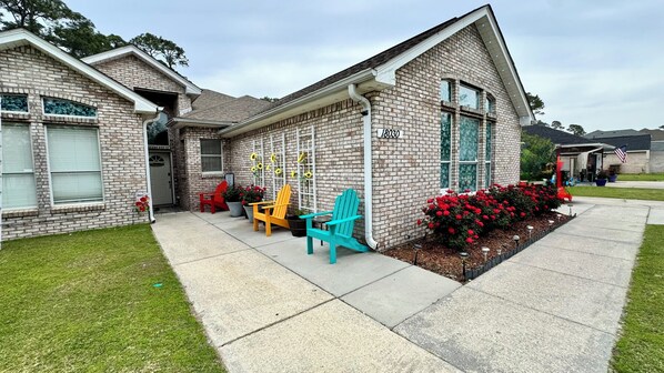 A brick house with a number 18030 on the side, a front porch with colorful Adirondack chairs, and a well-maintained lawn. - GaMe RoOm, Sleep 12, Colorful Back Yard, Beach(A) (Long Beach)
