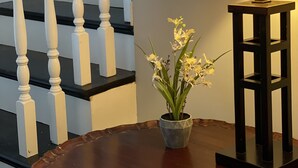 Eine Treppe mit weißen Balustraden und schwarzen Stufen, ein runder Holztisch mit Blumen in einer Vase und eine Stehlampe mit einer strukturierten Lampenschirm.