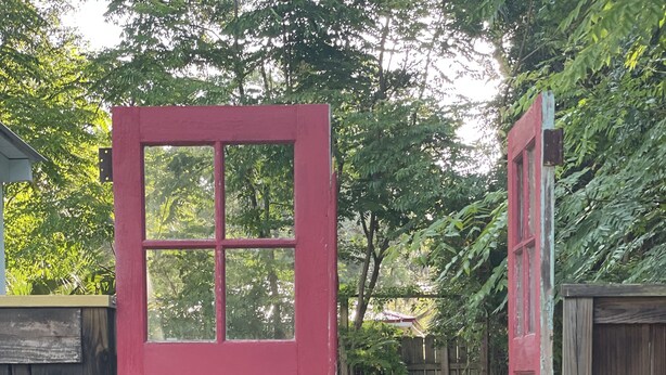 Eine rote Tür, die zu einem Holzdeck mit Gartenmöbeln führt.
