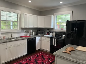 A modern kitchen with white cabinets, stainless steel appliances, and a red patterned rug. - Updated Victorian Red Door Revival in Downton St Aug (Saint Augustine)