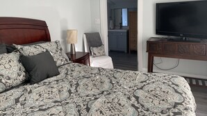 Ein Hotelzimmer mit einem großen Bett, einem Fernseher, einem Schreibtisch und Blick auf Küche und Bad.