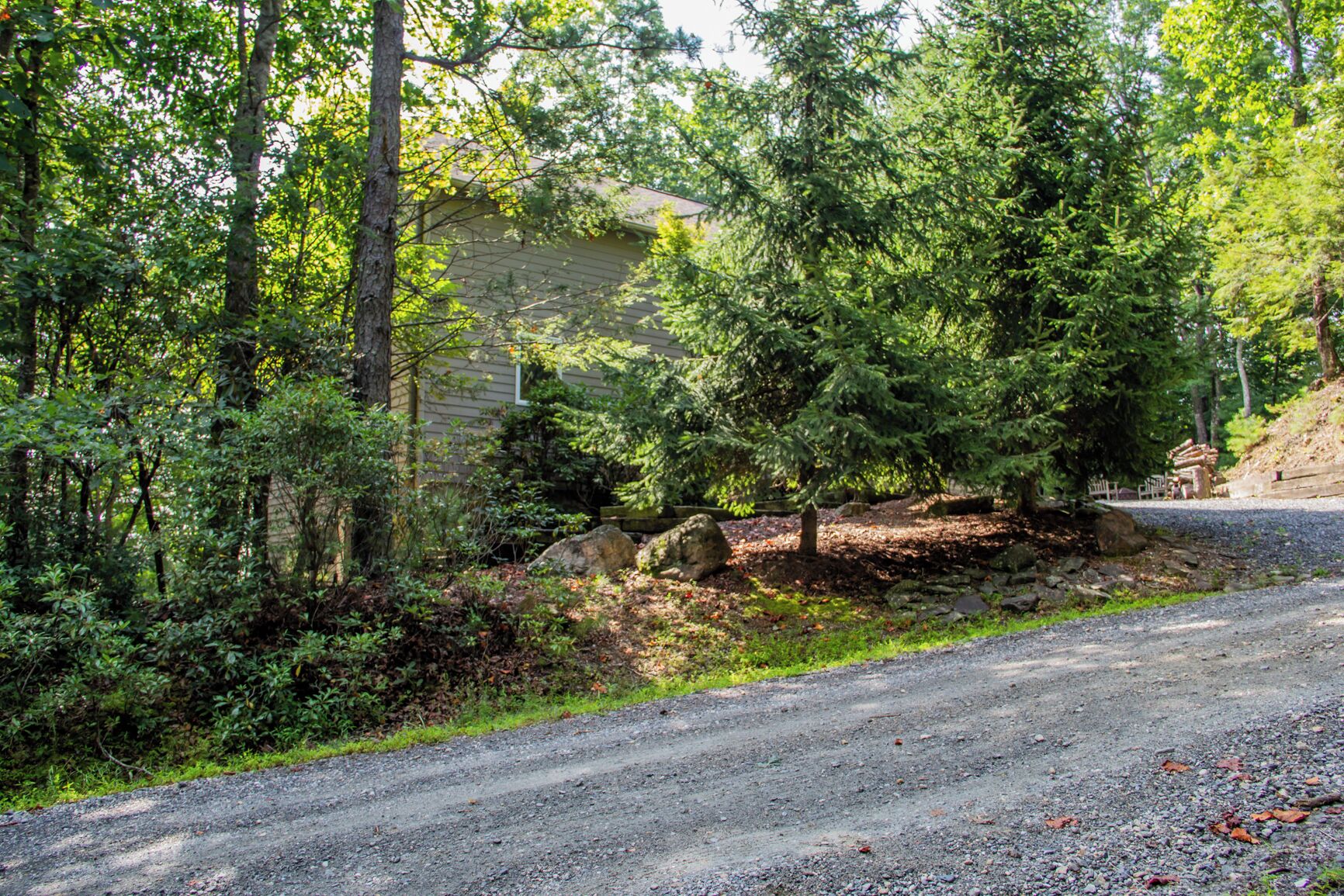 A gravel driveway leading to a house surrounded by dense trees and a stone wall.