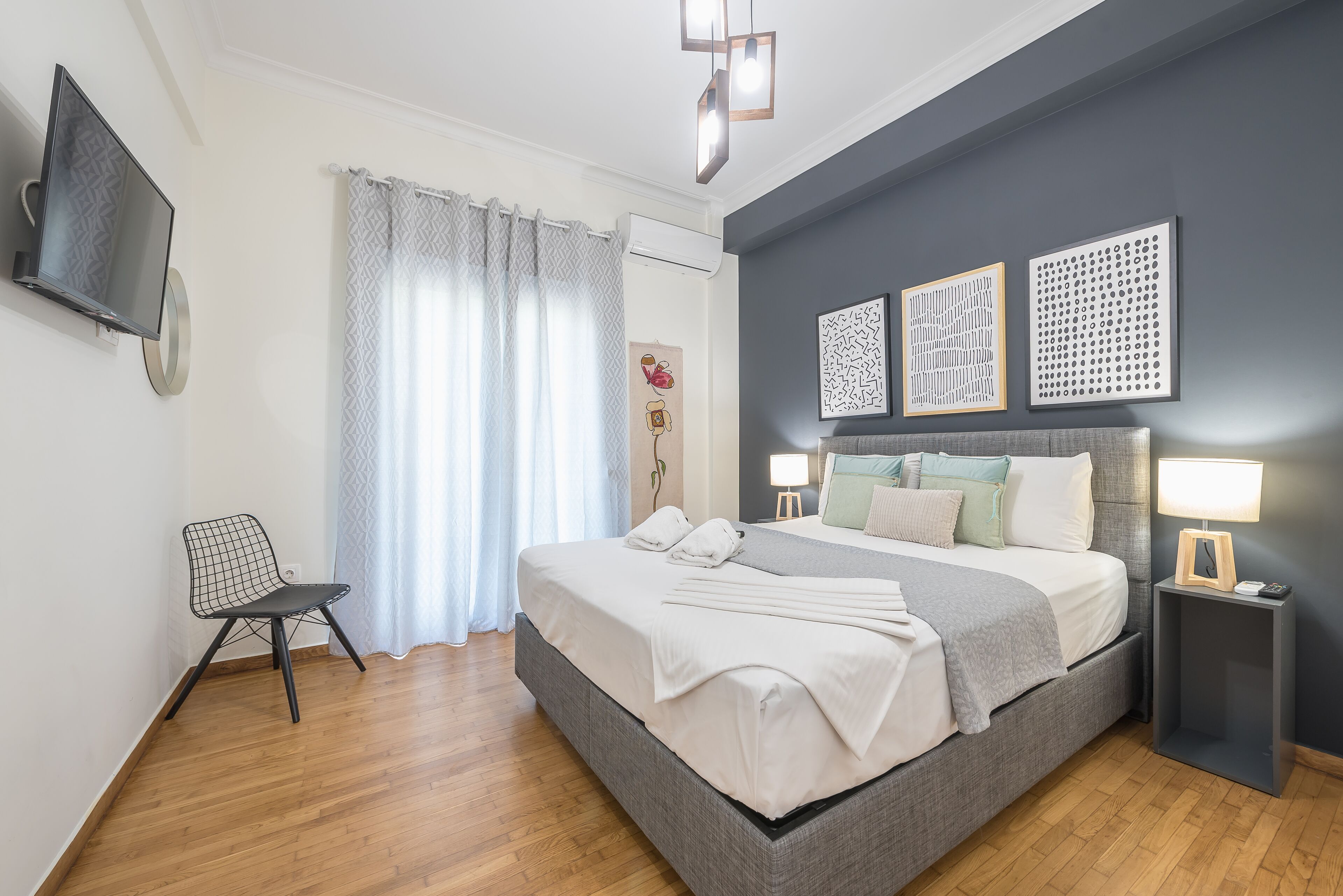 A modern bedroom with a large bed, a chair, a TV, and artwork on the wall.