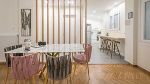 A modern dining area with a marble table, cushioned chairs, and a wooden partition. - Elegant Suite by CloudKeys (Athens)