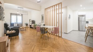 A modern living room with a sofa, coffee table, and a dining area with a table and chairs. - Elegant Suite by CloudKeys (Athens)