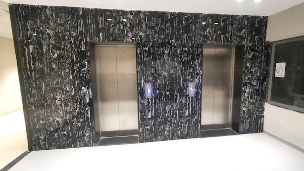Un ascensor moderno con pared de mármol negro y dos puertas metálicas.