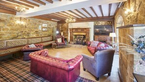 Un salon spacieux doté d’une cheminée, de poutres en bois, de murs en pierre et de fauteuils confortables.