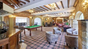 Une salle de billard équipée d’une table de billard, de sièges confortables et d’un mur en pierre rustique.