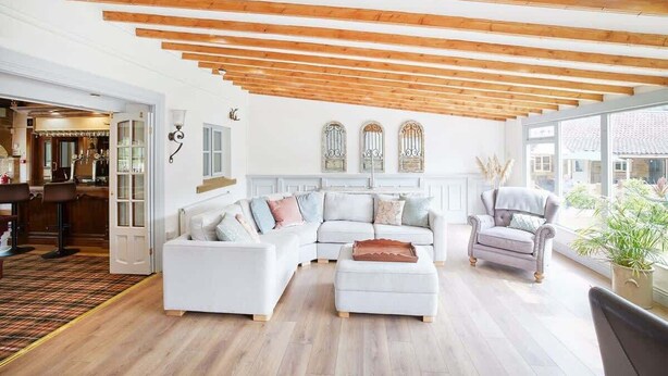 Un salon spacieux avec un canapé blanc, un petit fauteuil et un plafond en bois.