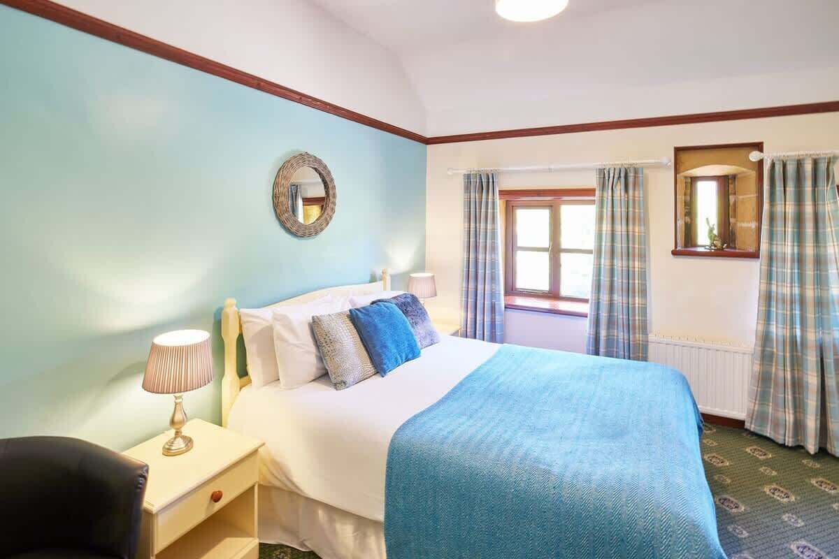 Una camera d'albergo con un letto, un comodino con una lampada, una sedia e una finestra con tende.