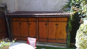 A patio with a round table and chairs, a wooden fence, and a small garden area with grass and plants. - Charming house for rent (Grilly)