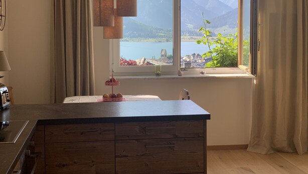 Eine Küche mit einer Holzeinsel, einem Fenster mit Blick auf Berge und einen See, sowie einer hängenden Pendelleuchte.