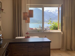 Una cocina con una isla de madera, una ventana con vistas a montañas y un lago, y una lámpara colgante.