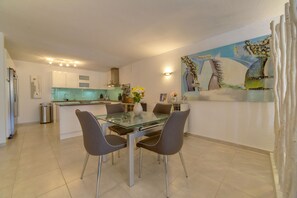Uma cozinha moderna com mesa de vidro, cadeiras cinzas e um quadro na parede.