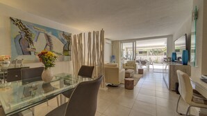 A modern living room with a glass dining table, comfortable seating, a large painting, and a view through a glass door. - Luxury Apartment, Fast WIFI, Large Terrace, Heated Pool, Marazul (Adeje)