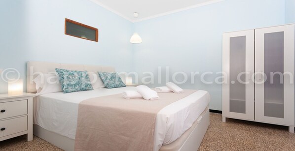 A bedroom with a bed, a nightstand, a wardrobe, and a wall-mounted light fixture.