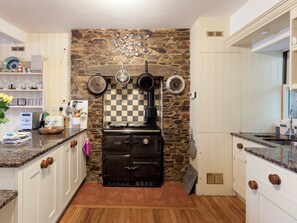 A kitchen with a stone wall, a stove, and various kitchen utensils.