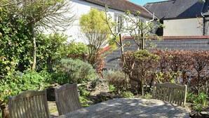 A wooden table and chairs in a garden with various plants and a white building in the background. - 4 bedroom accommodation in Market, Clarence & Sandquay (Market, Clarence & Sandquay)