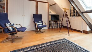 Ein Zimmer mit zwei blauen Sesseln, einem Teleskop, einem gemusterten Teppich und einem Bücherregal.