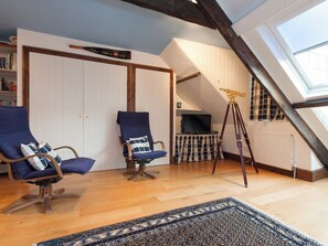 A room with two blue armchairs, a telescope, a patterned rug, and a bookshelf.