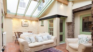 A cozy room with a high ceiling, a wooden ceiling beam, a stone wall, and a green door. There is a beige sofa with patterned cushions and a matching armchair. - 4 bedroom accommodation in Market, Clarence & Sandquay (Market, Clarence & Sandquay)