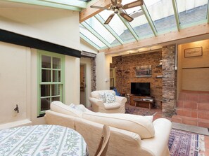Ein gemütliches Wohnzimmer mit Kamin aus Stein, Deckenventilator und großem Fenster.