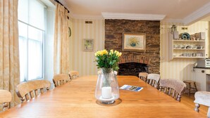 A dining room with a long wooden table, chairs, a vase with flowers, a fireplace, and a bookshelf. - 4 bedroom accommodation in Market, Clarence & Sandquay (Market, Clarence & Sandquay)