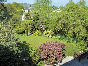 Un jardin avec une pelouse, un banc en bois et une variété de plantes et d’arbres.