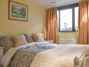 Un dormitorio con cama, mesita de noche, lámpara, ventana con cortinas y un cuadro en la pared.