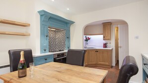 A dining area with a wooden table, chairs, a bottle of champagne, and a tiled backsplash. - 2 bedroom accommodation in Buckley St (Buckley St)
