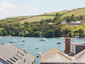 Un port avec des bateaux, une cheminée en briques et des maisons sur une colline.