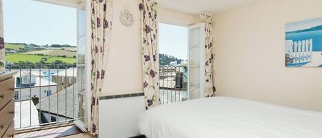 A bedroom with a bed, a dresser, a window with curtains, a clock, and a painting on the wall.