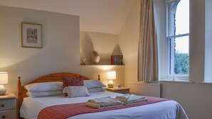 A neatly made bed with a red quilt, a bedside lamp, and a small vase on a nightstand. - 3 bedroom accommodation in Troutbeck Bridge (Troutbeck Bridge)