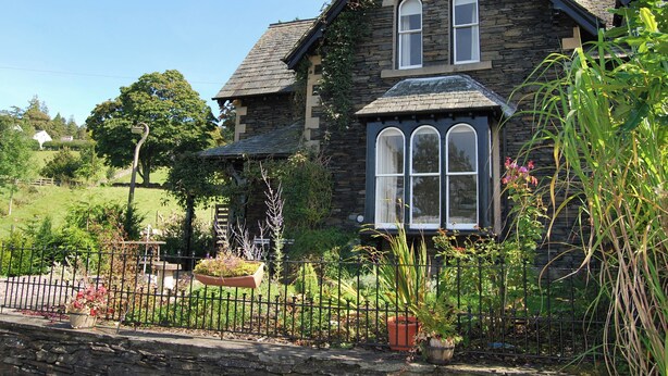 A stone house with a gabled roof, a chimney, and a large arched window. - 3 bedroom accommodation in Troutbeck Bridge (Troutbeck Bridge)