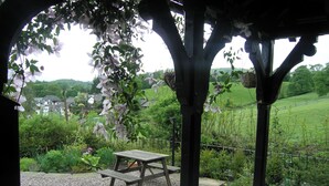 A gazebo with a picnic table surrounded by gravel, overlooking a lush garden and a distant village. - 3 bedroom accommodation in Troutbeck Bridge (Troutbeck Bridge)
