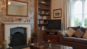 A living room with a fireplace, bookshelves, a television, and a sofa. - 3 bedroom accommodation in Troutbeck Bridge (Troutbeck Bridge)