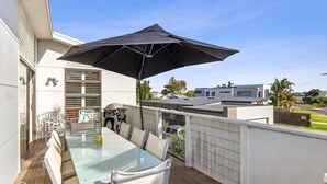 Un balcon avec une table en verre, des chaises, un barbecue et un grand parasol.