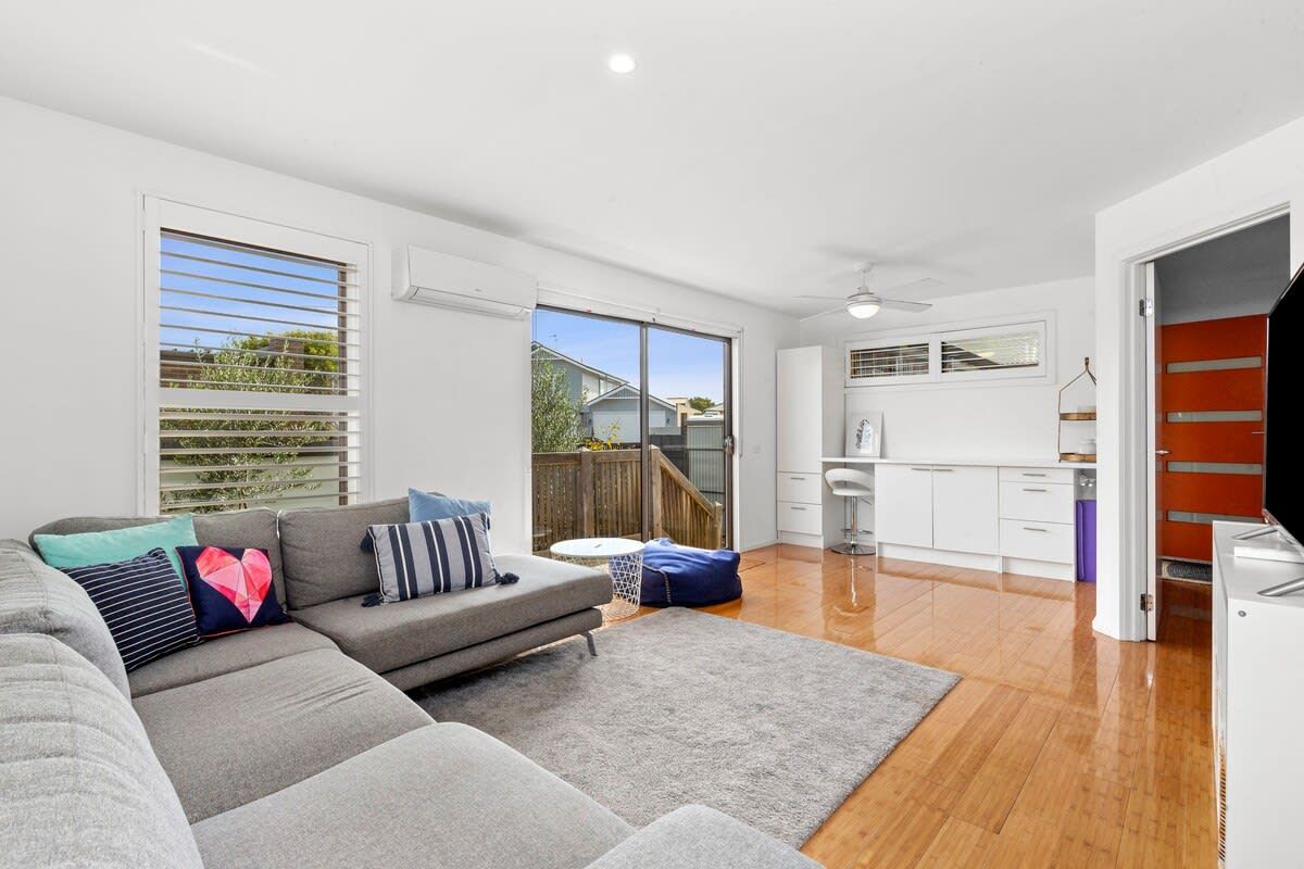A modern living space with a grey sofa, a kitchen area, and a staircase leading to an upper level.
