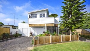 Une maison moderne à deux étages, dotée d’un garage, d’une clôture en bois et d’un grand arbre dans la cour.