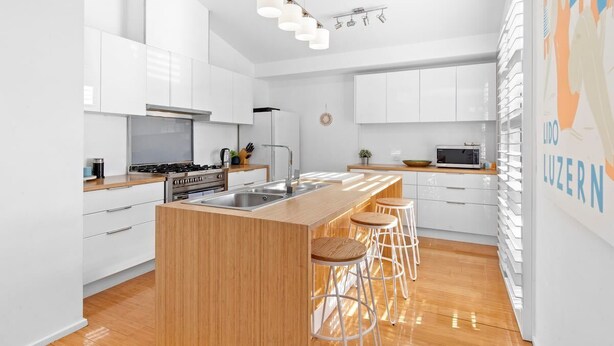 Une cuisine moderne avec des meubles blancs, un îlot central en bois doté de tabourets, un four à micro-ondes et un luminaire suspendu.