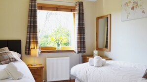 A hotel room with two beds, a window with plaid curtains, a radiator, a bedside table with a lamp, and a world map on the wall. - North Lodge Gate House (Muir of Ord)