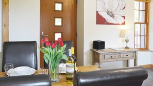 A dining area with a wooden table set for two, a vase of red tulips, and a bottle of white wine. - North Lodge Gate House (Muir of Ord)