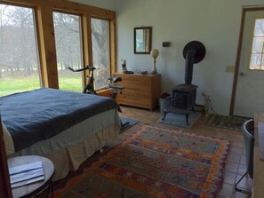 A bedroom with a bed, dresser, exercise bike, and a wood-burning stove.