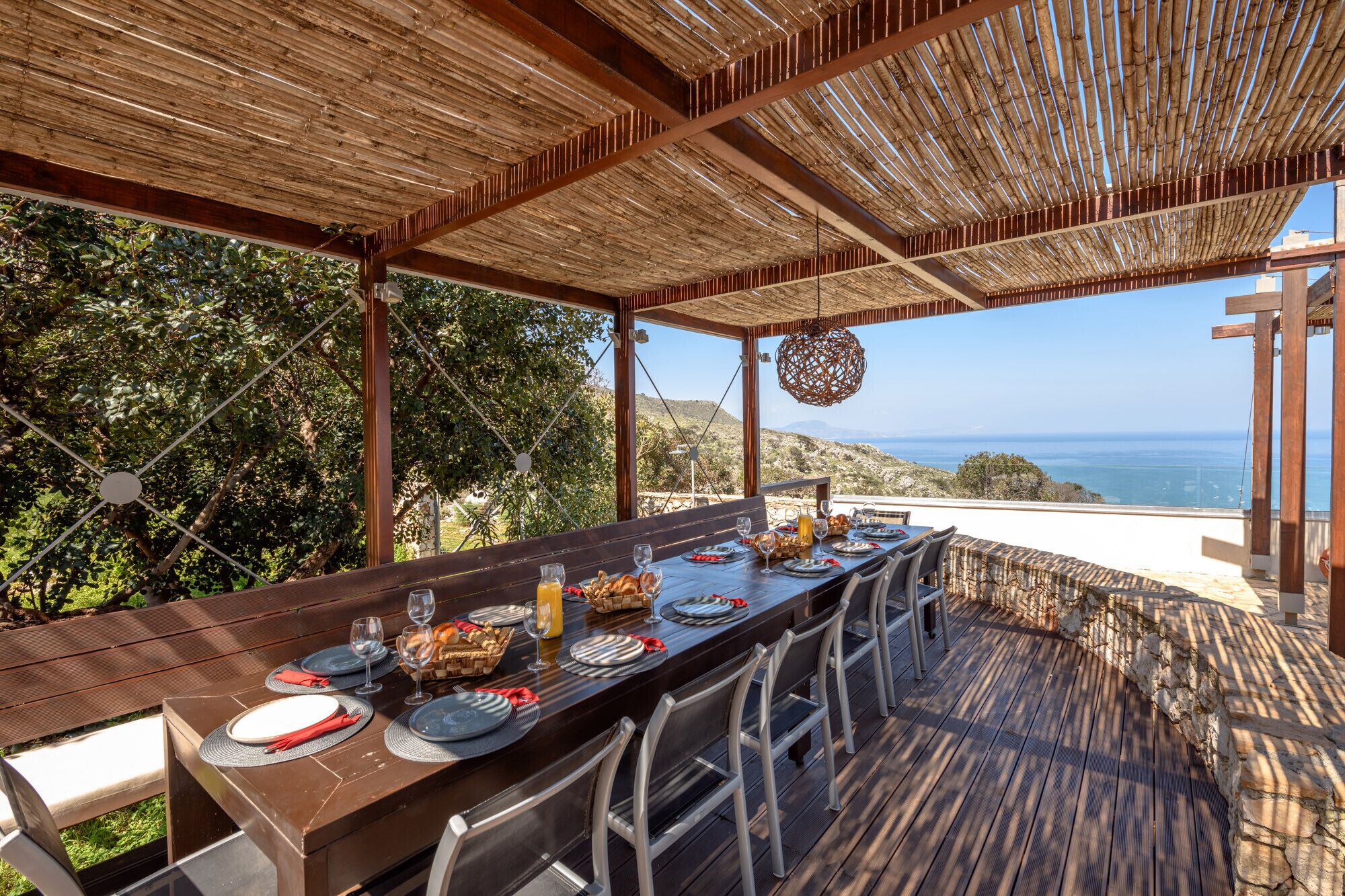 Un espace de restauration en plein air avec une longue table dressée pour un repas, offrant une vue panoramique sur la mer.