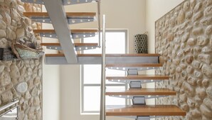 Un escalier moderne avec une structure en métal et des marches en bois, menant à un mur de pierre à motifs texturés.