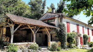 Un vieux bâtiment en pierre, avec un toit en tuiles, des poutres en bois et des volets rouges.