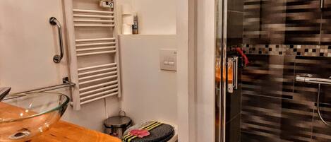 A bathroom with a glass bowl sink, a toilet with a decorative seat, a towel rack, and a shower area with a tiled wall.