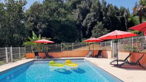 Une piscine à l’eau d’un bleu limpide, entourée d’une clôture métallique et dotée de parasols rouges.
